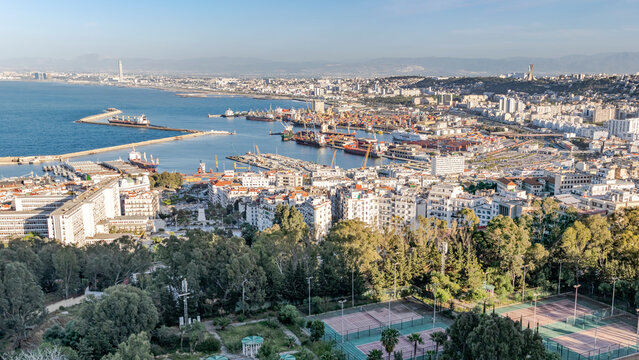 Algiers sea bay and pier port, aerial view on the capital city buildings, tennis court, trees and Mediterranean blue water ships and boats. The Great mosque and the Martyr's Memorial monument.