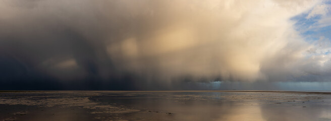Beautiful moody storm skies over ocean panorama landscape with distant heavy rainfall
