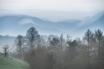 Stunning layered landscape image of misty Spring morning in Lake District looking towards distant misty peaks