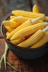 Tasty fresh yellow baby corns in bowl on wooden table, closeup