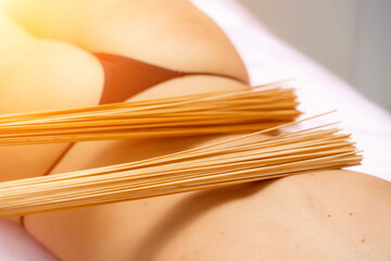 Woman masseuse doing double samurai massage with bamboo brooms in spa. Relaxing massage concept