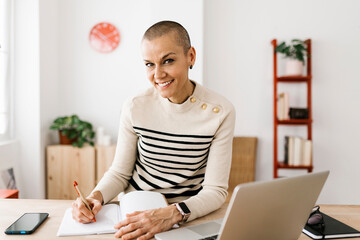 Portrait of mid adult businesswoman smiling at camera working with laptop at home office. Business...