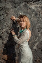 Middle aged woman looks good with blond hair, boho style in white long dress on the beach decorations on her neck and arms.