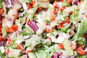 Greek salad background. Various ingredients lunch meal. Healthy vegetable snack. White feta cheese and honey vinegrette dressing. Crunchy lettuce and bell pepper. Raw vegetables.