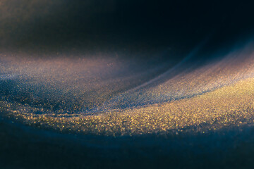 Blue and black acrylic paints with shimmering golden glitter. Liquid paint abstract background.