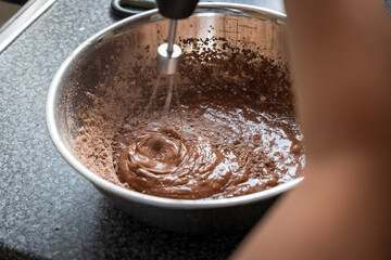 Child hands mixing ingredients in a bowl with a hand mixer on the countertop
