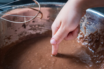 A childs finger emerges into chocolate cupcake mix in a bowl