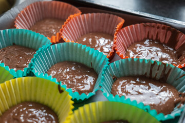 Chocolate cupcake mix sitting inside colorful baking liners inside baking tray ready for oven bake