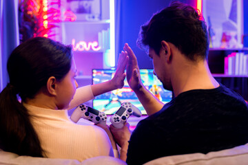 Couple or friend buddy joyful player video game on TV using joystick making hands high five at back...
