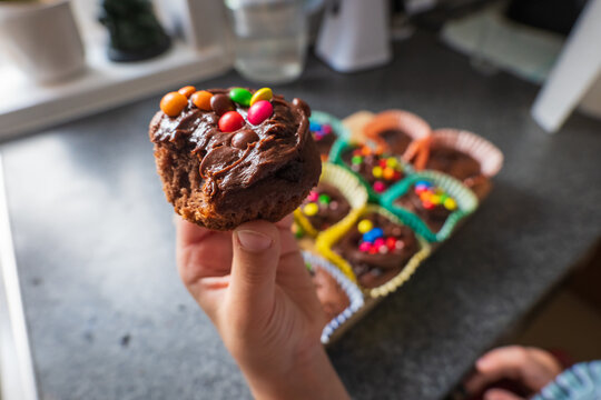 Child hand holding homemade chocolate cupcakes with chocolate chips and colorful sweets