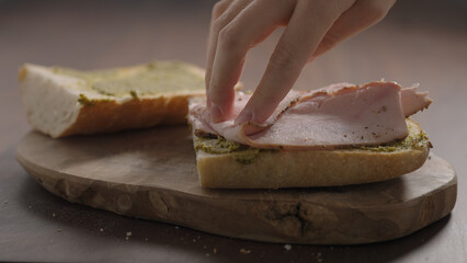 man making sandwich, add turkey slices on ciabatta on olive wood board