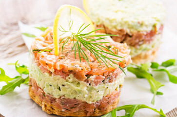 Gourmet salmon fish fruit tartar raw from salmon fillet with chopped avovado as close-up on a white...