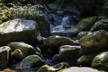 Gorgeous rocks lay on the river, water flowing between rocks full of moss and sunlight shines on it, in Nuandong Valley, Keelung city, Taiwan.