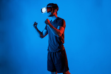 Happy man with VR goggle exercising and stretching arm at neon light background. Caucasian person...