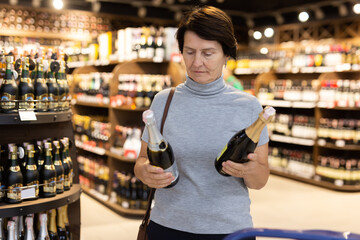 Mature woman choosing fine bottle of champagne in supermarket