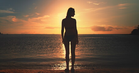 Woman stands on Koh Ma Beach at Koh Phangan Island in Thailand during sunset, with the sky painted...