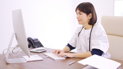 Doctor using computer sitting on a desk in a clinic