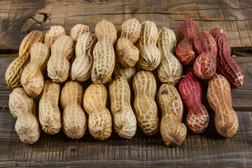 Peanuts with shells of different colors neatly lined up on a wooden table - obrazy, fototapety, plakaty