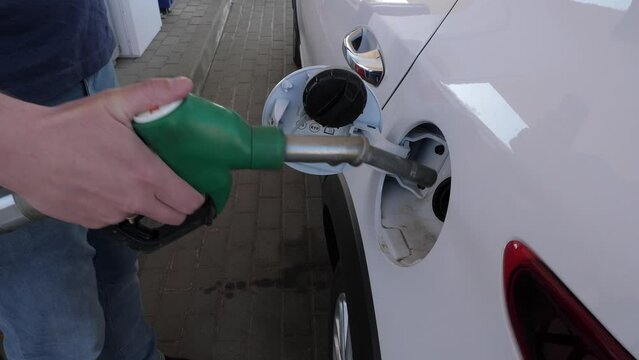 The man inserts a fuel pistol into the gas tank to refuel the car. A close-up of a man's hand inserting a fuel pistol into the gas tank to refuel a white car.