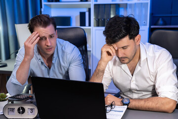 Stressful business partner with headache analyzing paperwork project together on desk at night time...