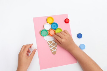 Ice cream cone craft on pink background, pastel process art, children playing with lids, top view.