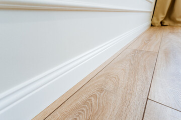 Closeup of a beige hardwood skirting board on wooden floor