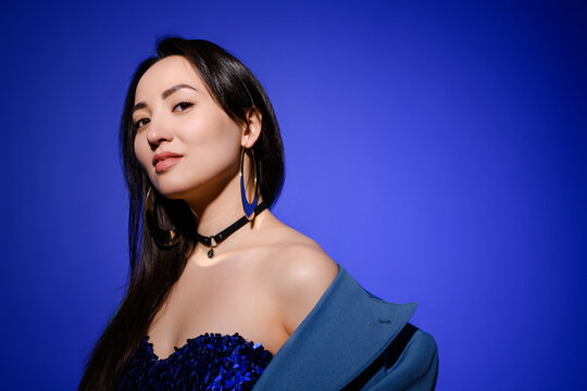 Portrait of confident and stylish asian woman in dress and choker isolated on blue 