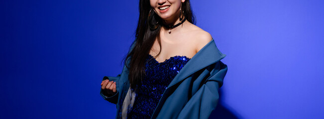 Banner crop of smiling and stylish woman in dress and jacket on blue background 