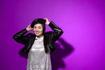 Smiling asian woman in dress wearing leather beret on purple background 
