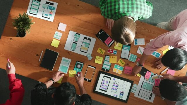 Top view of software developer team looking Ux Ui design for mobile phone interface from tablet while comparing and planning wireframe prototype designing together at creative workplace. Convocation.