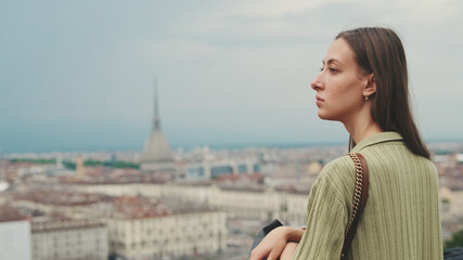 Young woman with brown hair wearing an olive green sweater looks at the city from the observation...