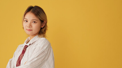 Young woman dressed in shirt and tie, crossing her arms and looking at camera isolated on yellow...