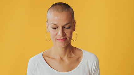 Close up, young hairless woman stands with her eyes closed, isolated on yellow background in studio