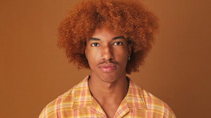 Close up, stylish curly guy looks at the camera, isolated on brown background in the studio