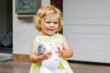 Little toddler girl playing with soft toy dog. Cute baby child holding toy and plays outdoors.