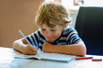 Portrait of happy boy doing homework in kitchen at home. Elementary school studing writing and...