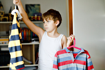 School kid boy standing by wardrobe with clothes. Child making decision for school shirt to wear....