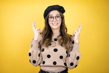 Young beautiful brunette woman wearing french beret and glasses over yellow background gesturing...
