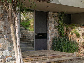 A modern design house stone paved entrance with a glass door and a view to the garden. Visit upscale neighborhoods of Athens, Greece.