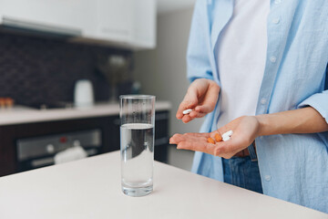 Woman taking medication with a glass of water and pill bottle on kitchen counter, healthcare concept