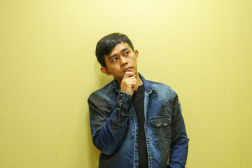 Obraz premium Portrait of a young man in a casual shirt and holding his hand on his chin, thinking about something and looking away on a yellow copy space background