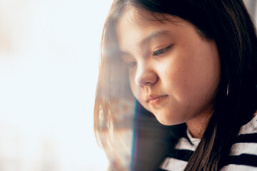young girl in striped sweater looks downwards, her expression soft and contemplative. gentle...