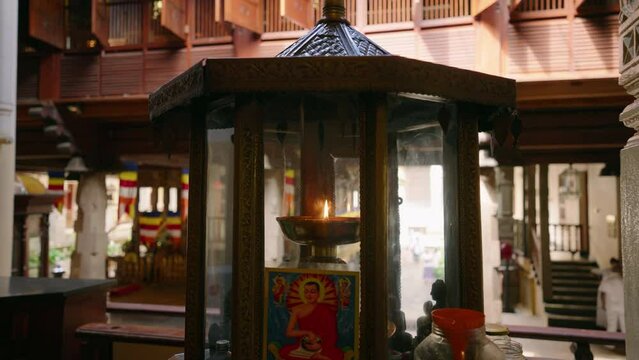 Aromatic oil lamp burns inside ancient Buddhist temple. Traditional carved lantern flickers, infuses ambiance. Visitors seek mindfulness, cultural heritage at Sri Lanka shrine.