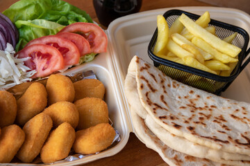 A tasty wrap sandwich featuring a medley of crisp onion, golden French fries, fresh green salad, and ripe tomato, all wrapped in a soft tortilla. Served with chicken nuggets on the side.