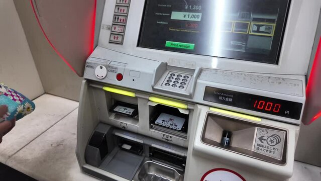 Closeup passenger hand adding Japanese yen into ticket vending machine at platform station and metro daily ticket pass, technology self buying ticket. Modern mass rapid transit system in Japan