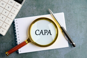 Concept words CAPA, corrective and preventive actions written through a magnifying glass on a...