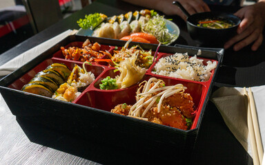 Japanese Lunch in Bento Box with Deep-Fried Squid Rings, Sushi Rolls, Salad, Rice, Pickled Ginger