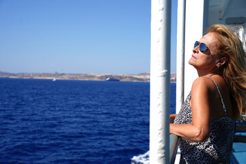 A woman tourist wearing sunglasses on a cruise looking out at the ocean.