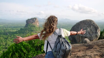 Mature asian woman spreads arms wide embracing freedom on rocky peak. Enjoys breathtaking view of Sigiriya Rock. Senior hiker celebrates achievement, solo travel adventure in nature. Slow motion.