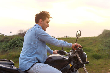 Curly haired Caucasian young man using his motorbike smiling and direct sunlight. Lifestyle concept